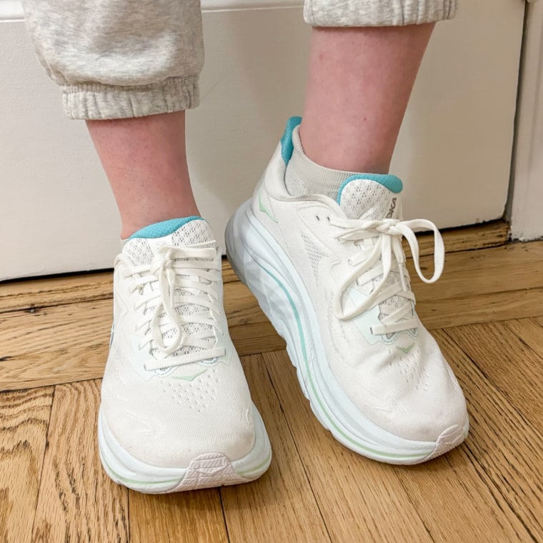 A woman wearing a white pair of Hoka Clifton 10 sneakers.